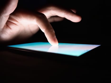 Hand touching on screen of smartphone on dark background.