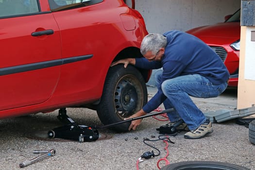 A man changes tires on a car. Changing winter tyres in autumn