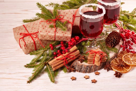 Still life with glasses of mulled wine or fruit tea, gift boxes, gingerbread cookies and christmas decorations on a wooden table. Christmas and New Year treat.