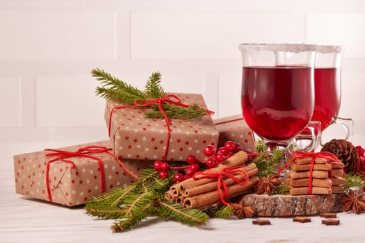 Still life with glasses of mulled wine or fruit tea, gift boxes, gingerbread cookies and christmas decorations on a wooden table. Christmas and New Year treat.
