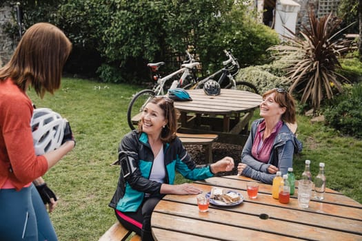 Three mature female adults meeting up to enjoy refreshments together at a park after a bike ride.