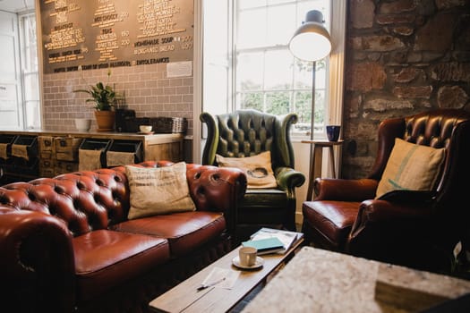 Empty interior of a small cafe, there is a seating area with leather sofas and a wooden table.