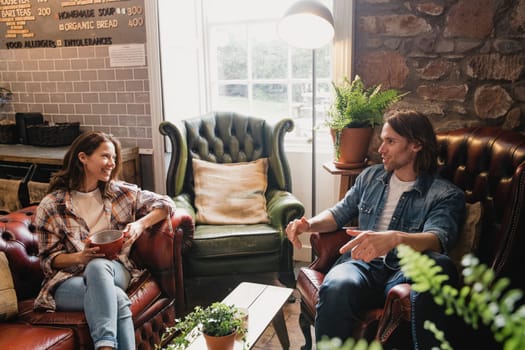 Mid-adult couple sitting in a small coffee shop relaxing. They are sitting on leather sofas and enjoying a coffee while talking.
