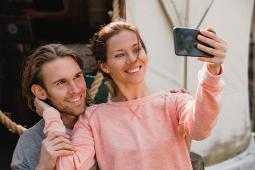 Mid-adult couple sitting outside looking and smiling at a smart phone as they take a selfie.