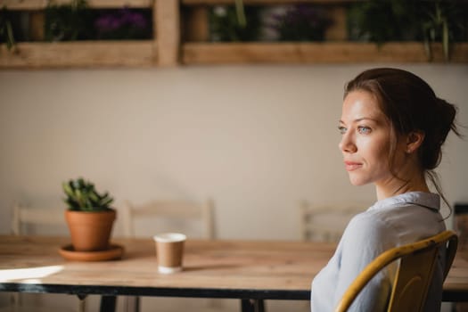 MId adult woman sitting at a take in a small cafe with a disposable coffee cup. She is looking out the window and enjoying the peace and quiet.