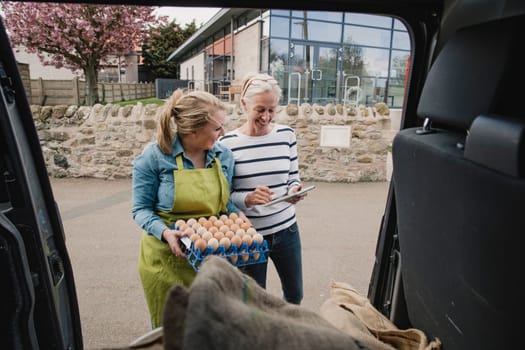 Mature female adult collecting a delivery off a young female adult outside from a delivery van.