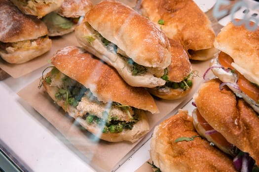 Stack of sandwiches in a coffee shop display cabinet. There is a variety to choose from.