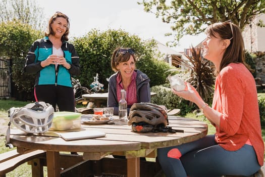 Small group of mature female cyclists sitting down in the outside seating area of a cafe. Tey are enjoying some refreshments as they take a break.