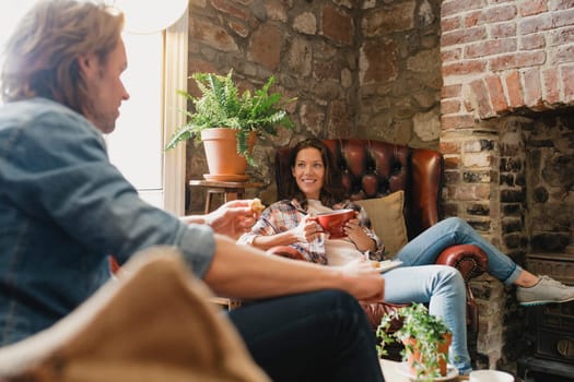 Mid-adult couple sitting in a small coffee shop relaxing. They are sitting on leather sofas and enjoying a coffee while talking.