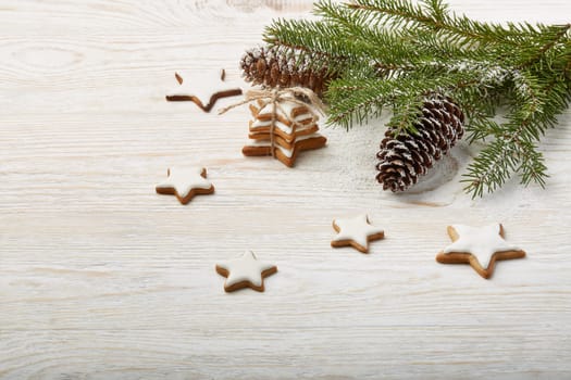 Light wooden background with fir branches, gingrebread cookies and cones. New Year and Christmas