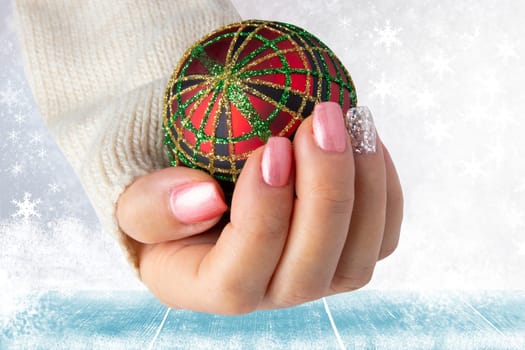 Beautiful female hand with christmas nail design. Hand with elegant pink nail manicure holding a red christmas decoration ball. Space for advertising.