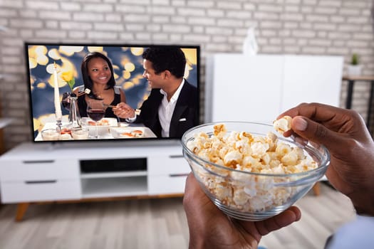 Close-up Of A Man Eating Popcorn While Watching Romantic Movie On Television