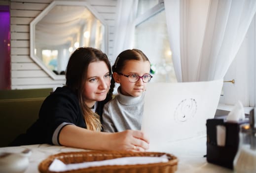 Family in a restaurant. Mother and daughter looking at restaurant menu. Selective focus.