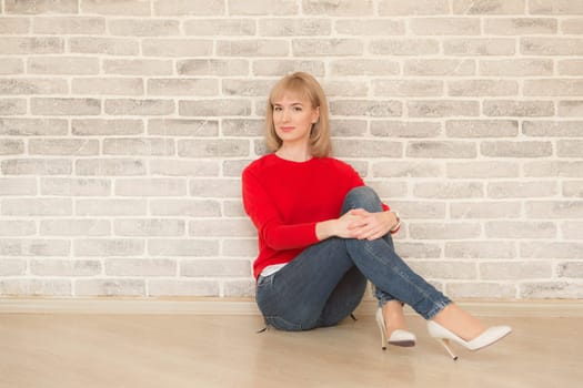 Happy girl smiling. Young happy positive woman in shirt sitting on floor in room on wall background. European woman. Positive human emotions facial expression body language