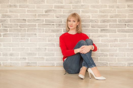 Happy girl smiling. Young happy positive woman in shirt sitting on floor in room on wall background. European woman. Positive human emotions facial expression body language