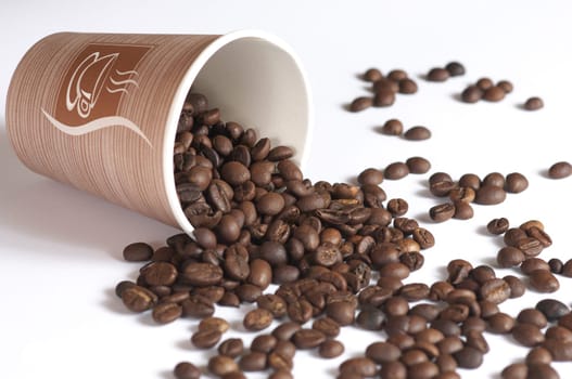 Dropped coffee beans. Coffee beans dropped into the paper. Glass with coffee beans dropped on white background.