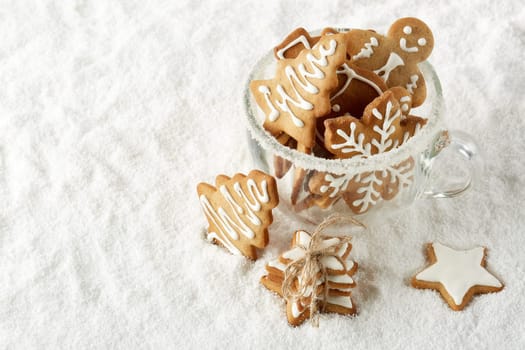 Handmade cookies in a glass cup standing on white winter snow background with copy space. Top view. New Year and Christmas.