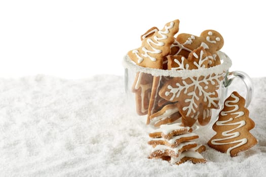 Handmade cookies in a glass cup standing on winter snow on a white background with copy space. Horizontal view. New Year and Christmas.