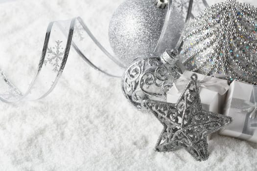 Christmas still life with silver balls, star and gift boxes lying on winter snow on a white background with copy space. Top view. New Year and Christmas.
