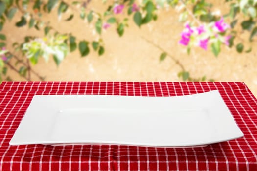 Empty plate background. Empty white plate on table with red napkin or tablecloth over yellow wall with flowers. Template for your food and product display montage. Concept food. Copy space.