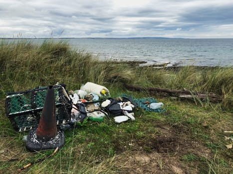 A wide-view shot of a polluted coastline, a heap of garbage can be seen on the grass which has been removed from the ocean.
