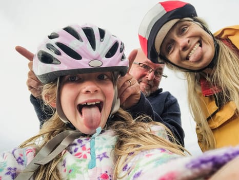 A close-up selfie of a happy family with one child, they are on an outdoor bikeride and pulling silly faces.