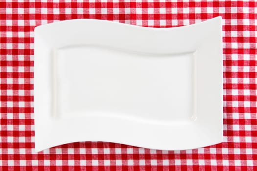 Empty white plate on red napkin or tablecloth. Top view. Template for your food and product display montage. Concept food. Copy space.