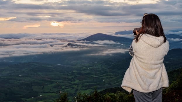 Woman tourist are using a DSLR camera photographing nature landscape the sun fog mountain in the winter during sunrise on high viewpoint at Phu Ruea National Park, Loei province, Thailand