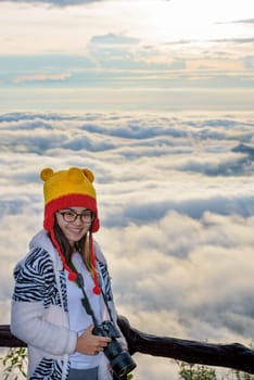 Woman tourist holding a DSLR camera on beautiful nature landscape of fog is like the sea in the winter during sunrise background at high viewpoint Phu Ruea National Park, Loei province, Thailand