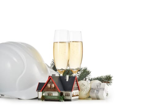 Construction hard hat, fir tree branches, model house, two glasses with champange and Christmas ornament isolated on a white background. Horizontal view with clipping path. New Year and Christmas.