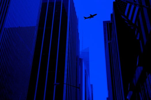 silhouetted flying commercial airplane above buildings.