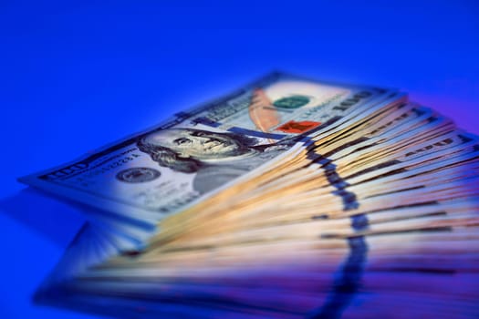 close up American hundred dollar bills pile under colorful lights