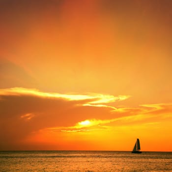 Orange color seascape image with shiny sea and sailboat over cloudy sky and sun during sunset in Cozumel, Mexico