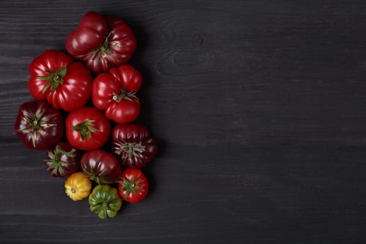 Different heirloom tomatoes on wooden black board as design background with copy space