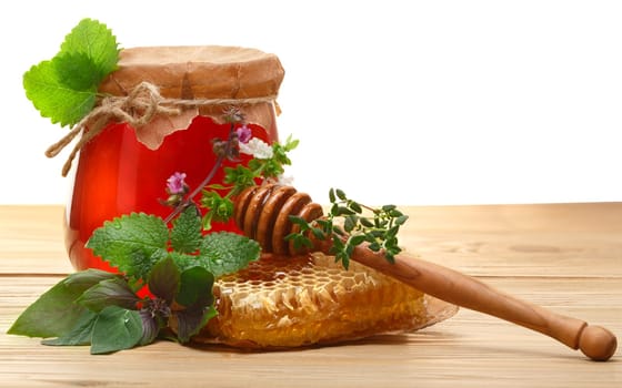 Glass jar of wildflower honey on wooden table next to honeycomb with honey dipper. Clipping path for background