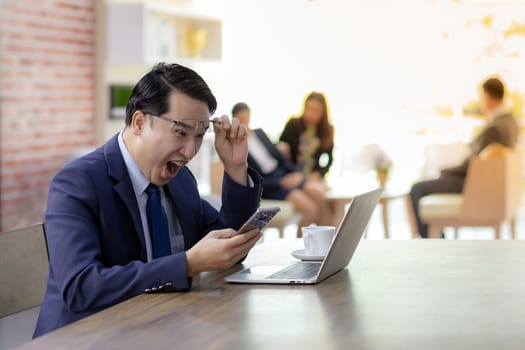 Portrait of Businessman celebrate his success in cafe with smart phone and tablet with business team in background using for coporate background work