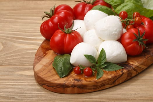 Italian cuisine. Mozzarella, heirloom tomatoes, basil leaves on a wooden serving plate. Selective focus on cheese