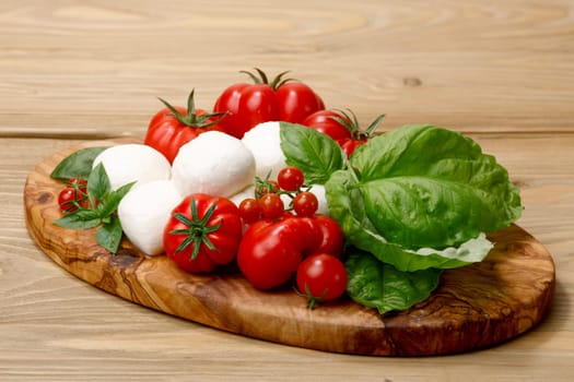 Italian cuisine. Mozzarella, heirloom tomatoes, basil leaves on a wooden serving plate. Selective focus on cheese