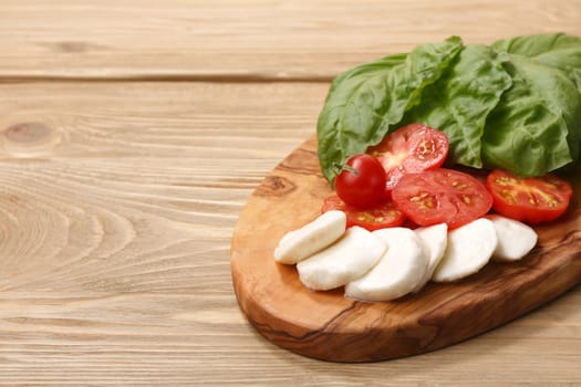 Italian cuisine. Sliced Mozzarella, heirloom tomatoes, basil leaves on a wooden serving plate. Selective focus on cheese