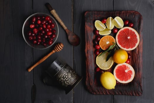 Ingredients for hot winter punch,sangria,toddy or mulled wine. Sliced lemon, grapefruit,tangerine, lime and cranberry on a rustic wooden tray over black wooden backdrop
