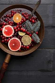 Hot winter punch,sangria,toddy or mulled wine with lemon, grapefruit,tangerine, lime and cranberry in aged rustic brass pot over black wooden table