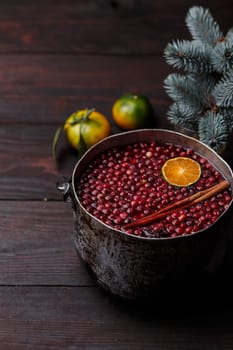 Cranberry mandarin pomegranate punch or mulled wine in a rustic aged pot near blue spruce branch