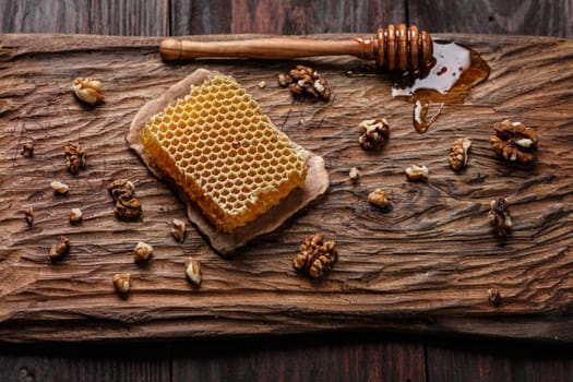 Honey dip, honeycomb and walnuts on carved wooden serving plate over burnished wood table