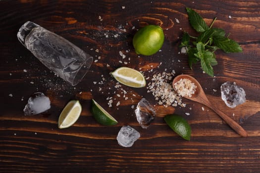 Ingredients for mojito on dark wooden table. Lime, spoon of rough cane sugar,mint,ice cubes and highball