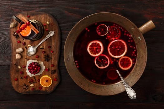Cranberry citrus punch or mulled wine with ingredients over dark wooden table.