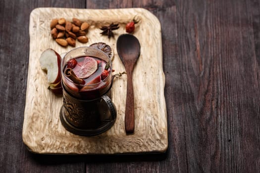 Hot Toddy (mulled wine, punch) with apples and rose hips served on rustic wooden tray with almonds over dark wooden table