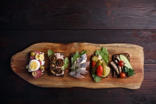 Variety of open sandwiches of buttered dense, dark rye bread with different toppings. Danish smorrebrods on wooden backdrop. Northern cuisine