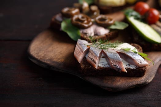Variety of open sandwiches of buttered dense, dark rye bread with different toppings. Danish smorrebrods on wooden backdrop. Northern cuisine. Selective focus
