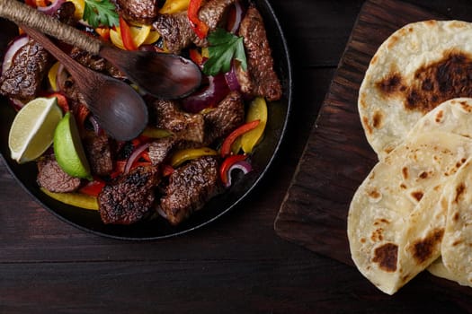 Beef fajita with bell peppers. Tortillas, avocado, sauce served with grilled beef and vegetables on skillet. Tex-mex cuisine
