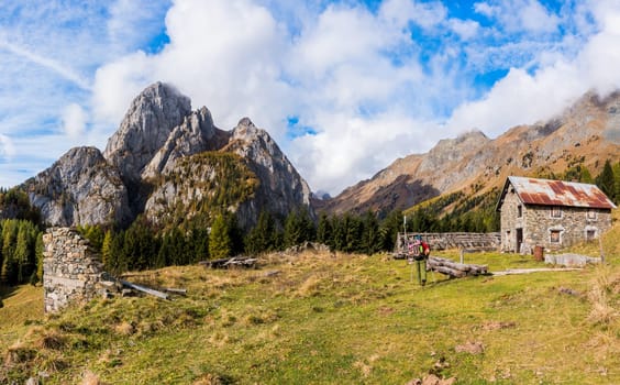 Mountain landscape with blue sky with clouds and ruins of an old farm and a hiker